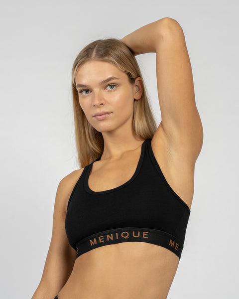 Mujer vistiendo un sujetador deportivo negro de lana merina con diseño de espalda cruzada, posando con un brazo levantado.