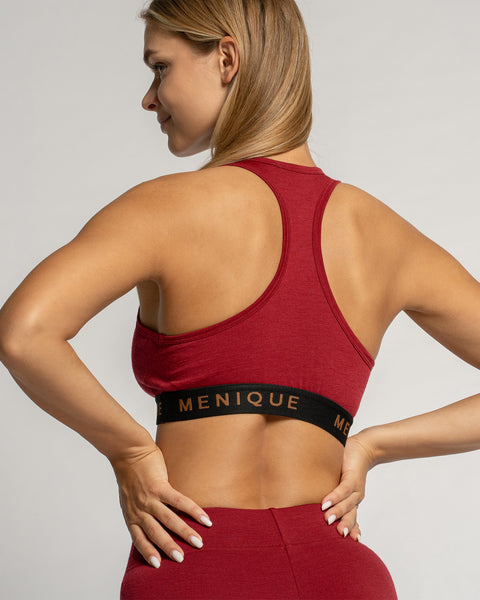 Mujer vistiendo un sujetador deportivo rojo y mallas con la marca 'Menique' sobre un fondo gris claro