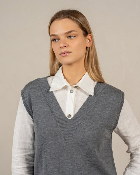El chaleco de lana merina menique ISLA en color gris. El modelo mira hacia un lado, el chaleco tiene un escote en pico y una silueta relajada.