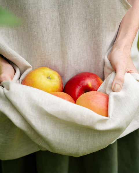 Un primer plano de manos recogiendo manzanas en los pliegues de un delantal de lino natural.