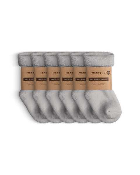 Seis pares de calcetines de forro polar sherpa gris claro para niños, doblados cuidadosamente con etiquetas de papel marrón Menique marcadas con ‘Calidad Premium’.