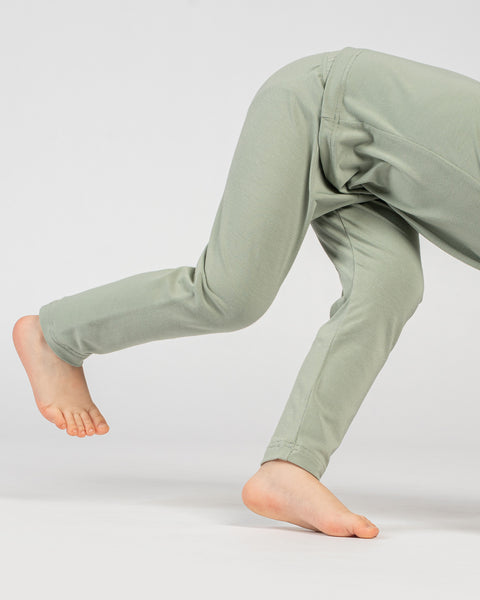 Vista lateral en primer plano de las piernas de un niño con pantalones verdes de bambú mientras juega.