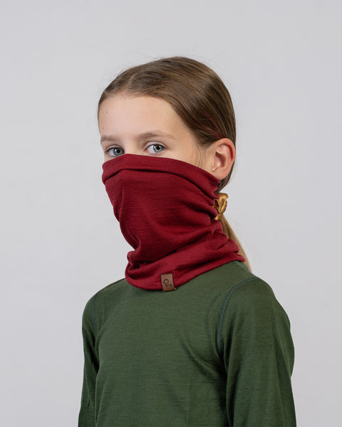 Niña con camiseta verde que lleva un braga de cuello de lana merina roja: ropa de invierno versátil y cómoda para niños.