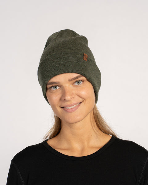 Mujer con un gorro de lana merina tejido de color verde oscuro, sonriendo y mirando al frente, con una camiseta negra.