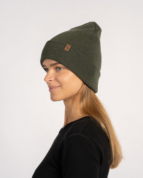 Mujer con un gorro de lana merina tejido de color verde oscuro, girada de lado hacia la izquierda, mostrando el perfil del sombrero.