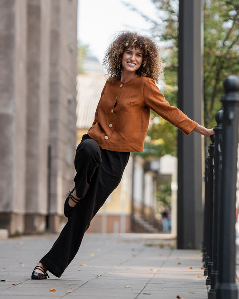 Mujer con cabello rizado que lleva una chaqueta de lino color almendra Alice y está de pie en una calle