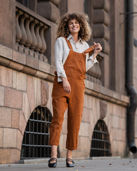 Woman with curly hair standing in a street and wearing Linen Pinafore Jumpsuit Nicci Almond Brown