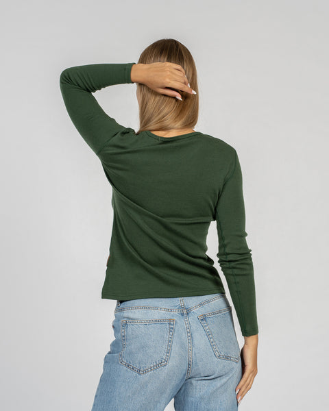 La camiseta de manga larga para mujer de menique en lana merina verde oscuro combinada con vaqueros clásicos azul claro, vista trasera.