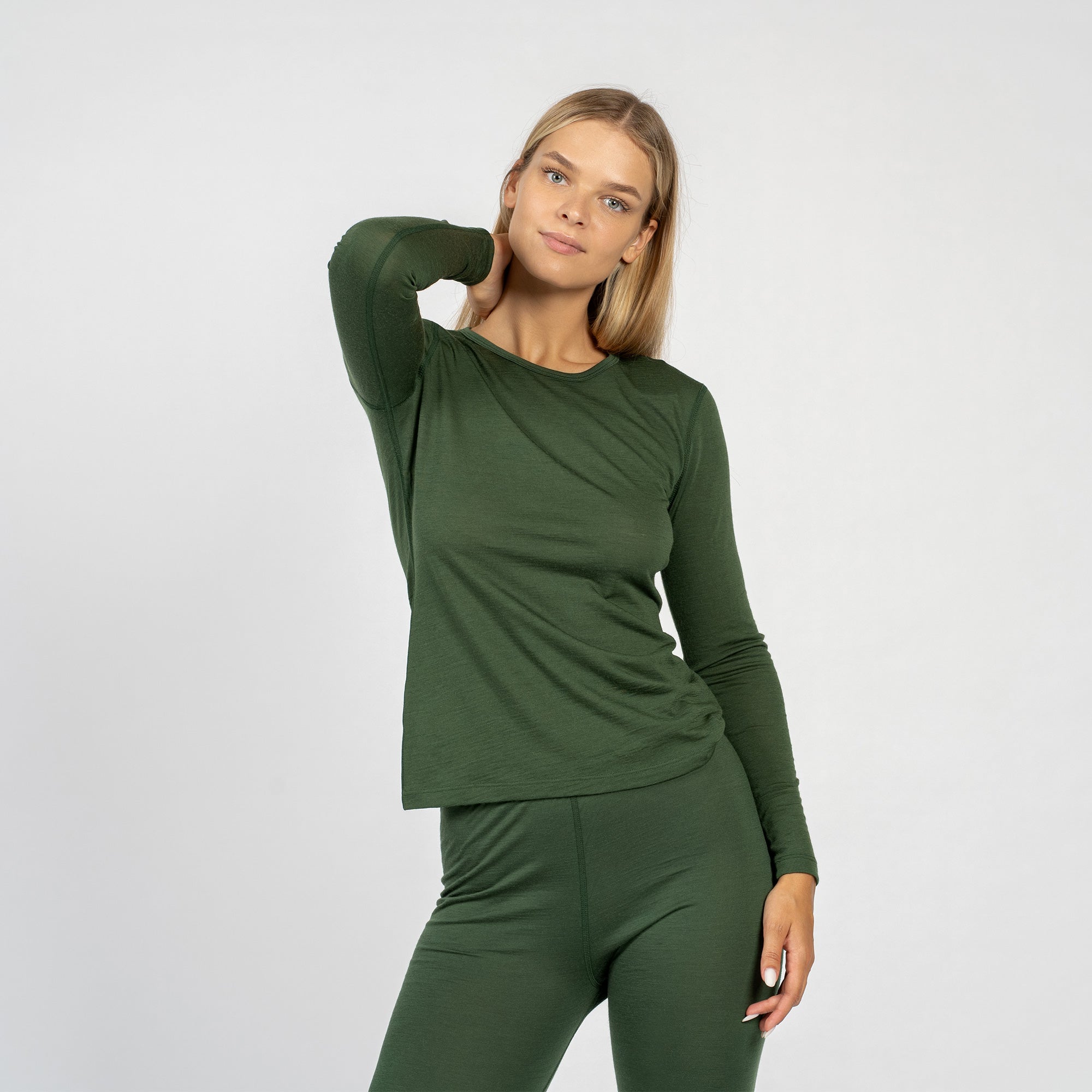 La camiseta de manga larga para mujer de lana merina en verde oscuro de menique combinada con los pantalones verdes oscuros de menique, vista desde el frente.