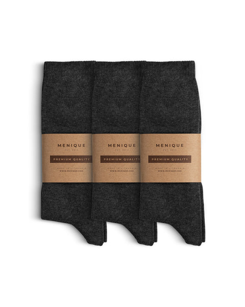 Juego de tres pares de calcetines de algodón para hombre en gris oscuro, cuidadosamente doblados y envueltos con el embalaje minimalista de papel kraft marrón de Menique, etiquetado como ‘Calidad Premium’.