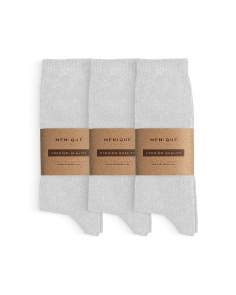 Tres pares de calcetines blancos de algodón para hombre, doblados cuidadosamente y envueltos con bandas de papel marrón de Menique etiquetadas como ‘Calidad Premium’.