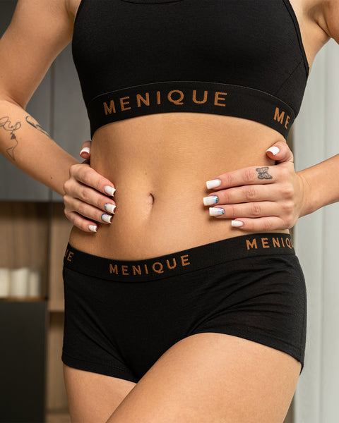 una mujer que lleva puestos unos calzoncillos bóxer negros de merino para mujer, con las manos apoyadas en la cintura. También lleva un sujetador a juego.
