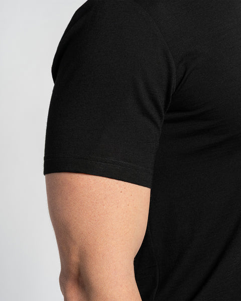 Primer plano de la manga de una camiseta negra de merino, mostrando la textura de la tela y los detalles de la costura. La camiseta se muestra en el brazo de una persona, con un fondo claro.