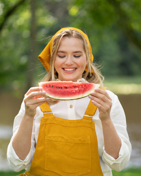Woman in yellow Nicci linen jumpsuit holding a watermelon slice outdoors