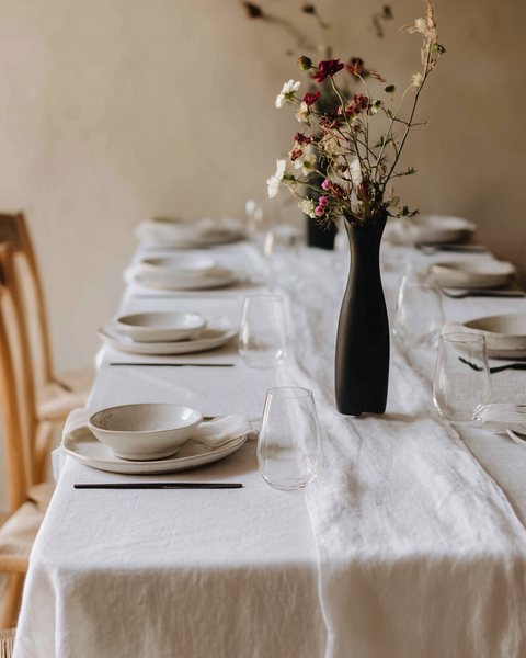 Mantel de lino blanco puro con una mesa minimalista y vajilla de cerámica para una cena elegante.