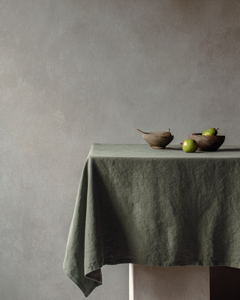 Mantel de lino verde piedra con decoración natural minimalista y cuencos de cerámica texturizados.