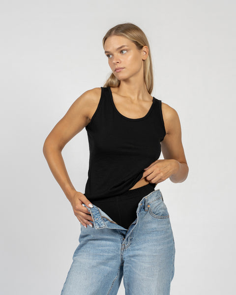 Camiseta sin mangas negra de lana merina para mujer, usada como capa térmica base bajo jeans, ligera y transpirable