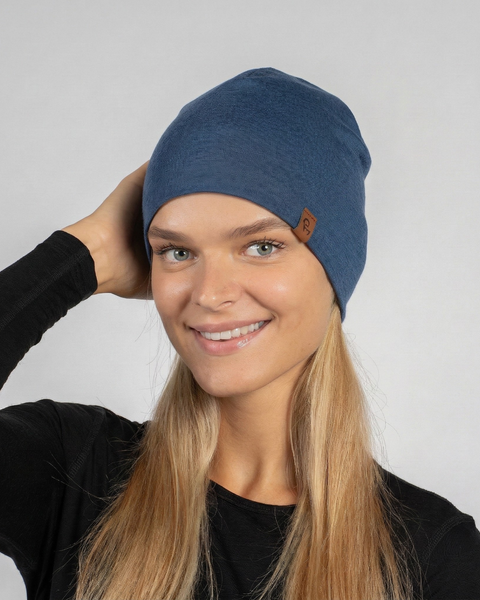 Woman wearing denim blue merino wool liner beanie, lightweight merino wool hat designed for comfort and active outdoor lifestyle.