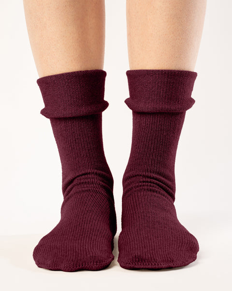 A straight-on view shows a person from the mid-thigh down, wearing ribbed, royal cherry color socks with a folded-down cuff. The socks extend to the mid-calf, and the person's feet are positioned slightly apart on a plain white background. The lighting is uniform, highlighting the texture and folds of the socks.