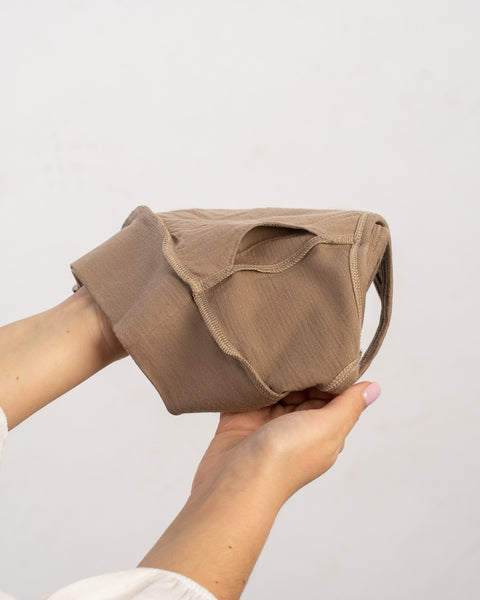 Manos sosteniendo un bralette marrón claro, posiblemente hecho de tela suave y ligera, contra un fondo claro y liso.