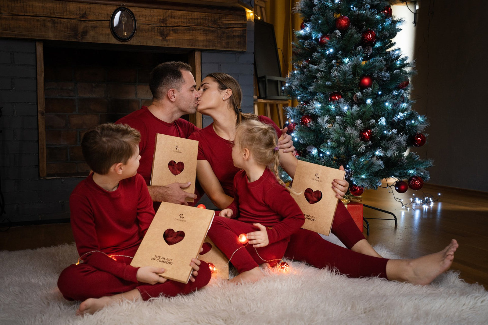 Familia feliz sentada cerca de un árbol de Navidad con ropa a juego de color rojo y intercambiando regalos.