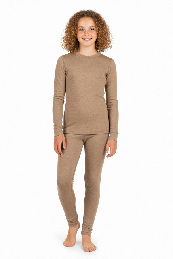 Una niña que lleva una camiseta interior de manga larga de lana merina beige y leggings a juego, de pie descalza y sonriendo frente a un fondo blanco de estudio.