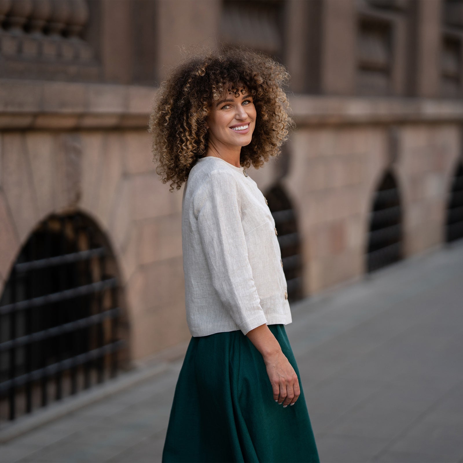 Un modelo que lleva una chaqueta Alice de lino beige natural con botones, con un corte holgado, mangas tres cuartos y un diseño minimalista. La chaqueta se combina con una falda a juego de color verde oscuro.