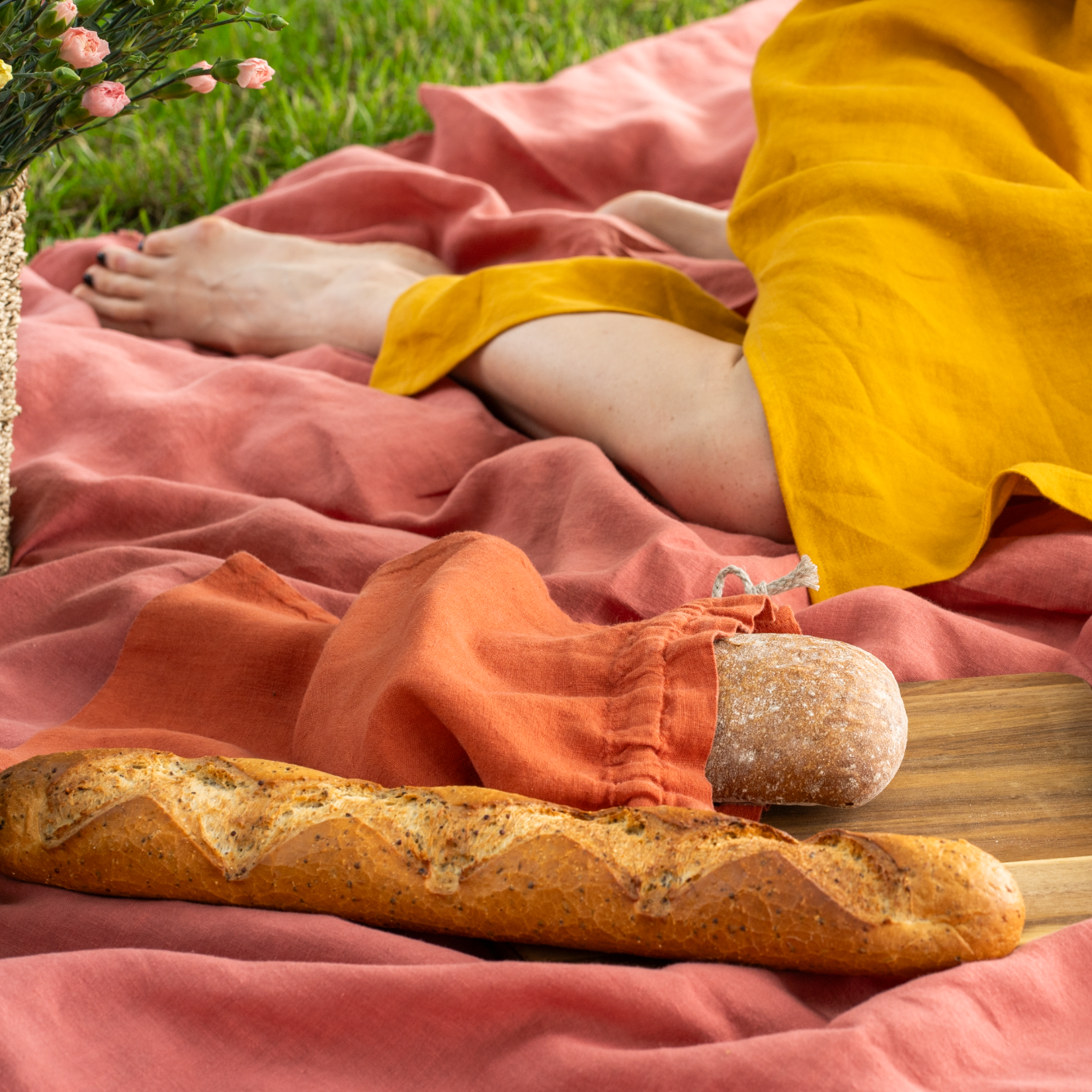 Bolsa reutilizable de lino para pan y baguette en color rojo canela sobre una manta y una tabla de madera.