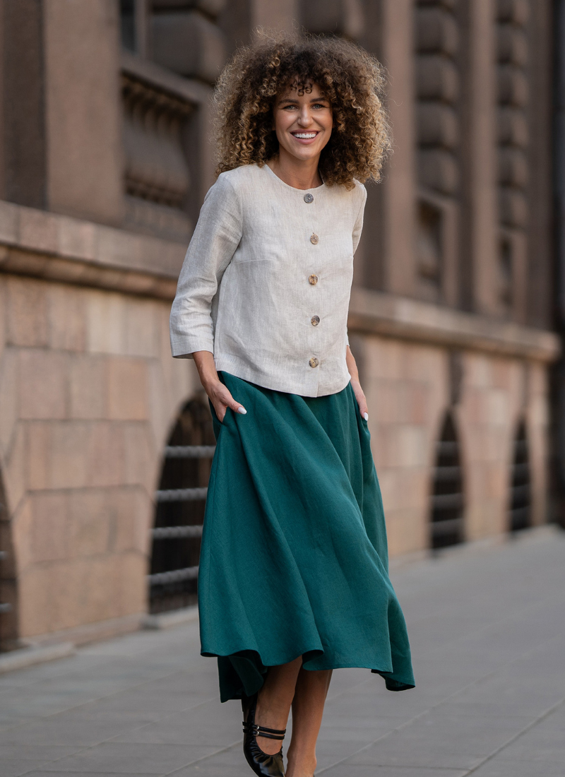 Woman wearing linen blouse and green skirt walking outdoors in the city.