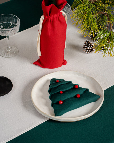 Una mesa navideña con un plato encima, con la servilleta de lino menique en color verde oscuro doblada en forma de árbol de Navidad.