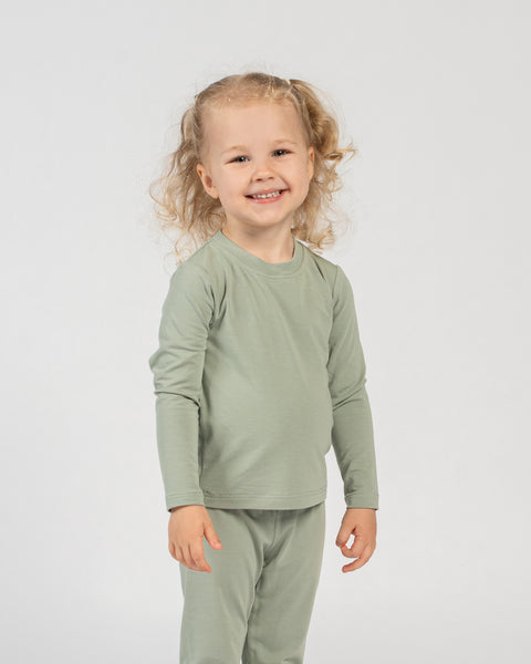 Smiling child standing in green bamboo long-sleeve top and bottoms, front view.
