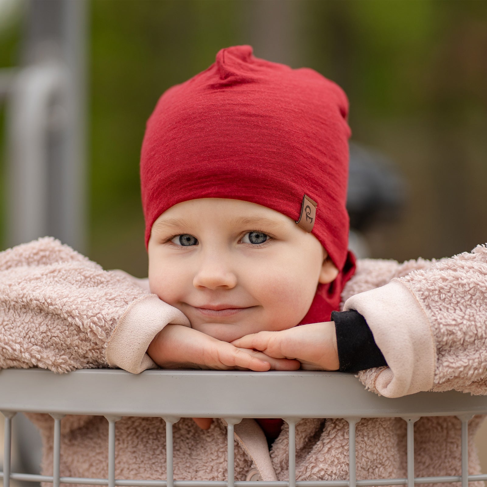 Niño sonriente jugando al aire libre con un gorro negro de lana merina para niños y un braga de cuello a juego, abrigo beige acogedor, fondo de parque infantil.