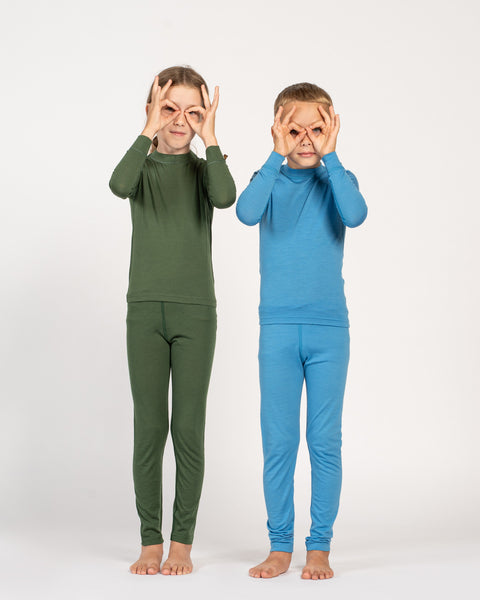 Dos niños vistiendo pijamas verdes y azules sobre un fondo blanco