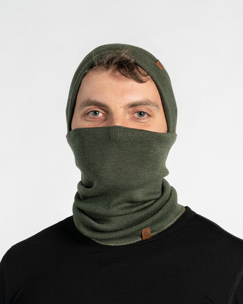 Hombre con un braga de cuello y gorro tejidos de lana merina menique de color verde oscuro sobre un fondo blanco