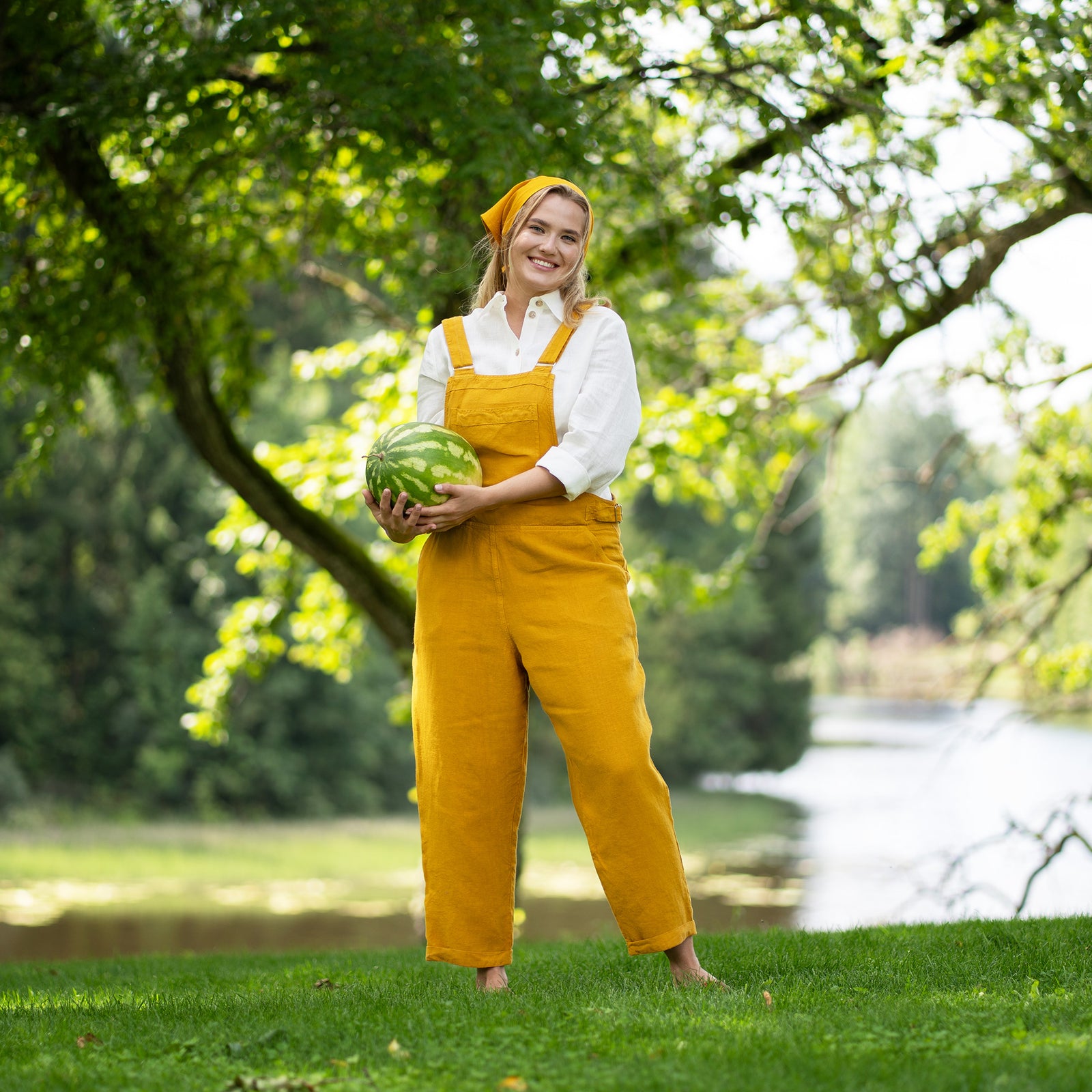Mujer con mono amarillo Nicci de lino sosteniendo una rodaja de sandía en un entorno similar a un parque