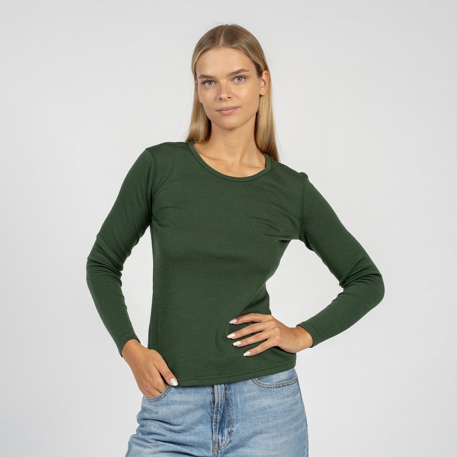 La camiseta de manga larga para mujer de lana merina en verde oscuro de menique combinada con los pantalones verdes oscuros de menique, vista desde el frente.
