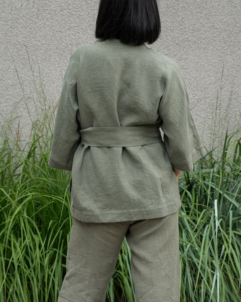 Mujer de cabello corto y oscuro que lleva una chaqueta de lino verde piedra y pantalones menique verde piedra, vista desde atrás.