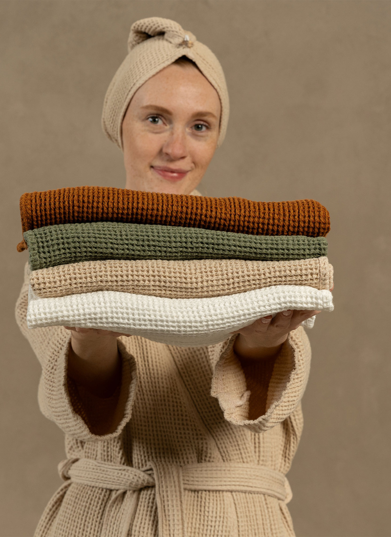 Woman holds a thick, multi-colored knit textile—featuring bands of forest green, mustard, and cream—up to her face.