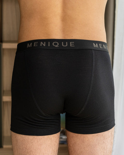 Un hombre lleva puestos calzoncillos bóxer cortos hechos de tela de lana merina, en color negro. En la fotografía se ve la parte trasera de los calzoncillos bóxer.