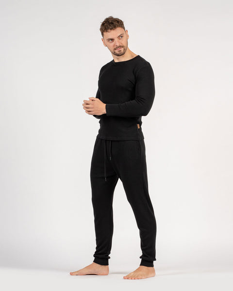 El conjunto para hombre de menique, compuesto por camiseta de manga larga de lana merina de 250 g/m² y pantalones deportivos tipo jogger en color negro.
