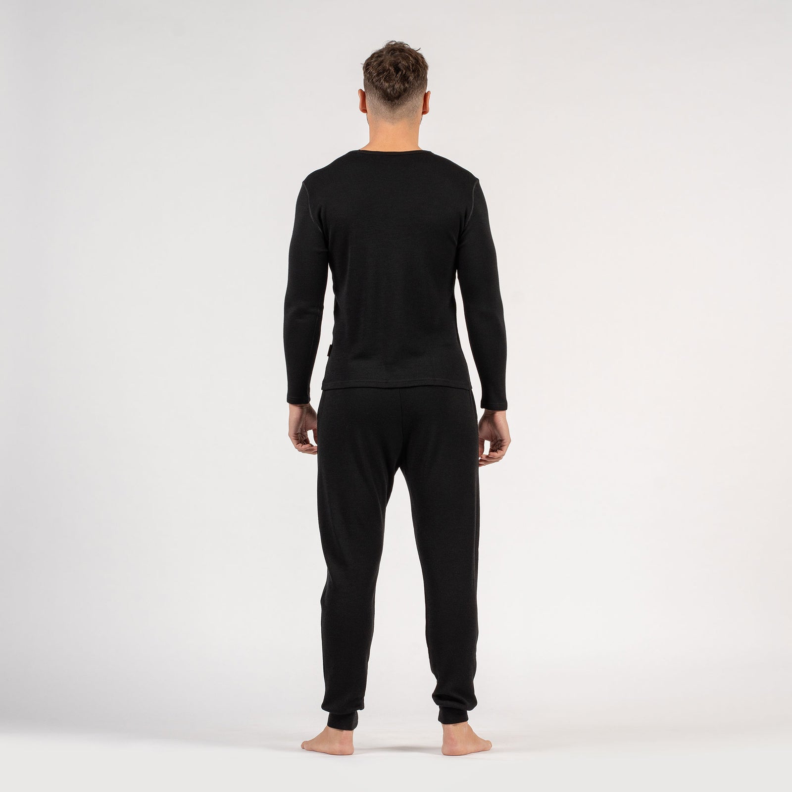 El conjunto para hombre de menique, compuesto por camiseta de manga larga de lana merina de 250 g/m² y pantalones deportivos tipo jogger en color negro.