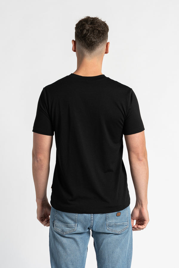 Vista trasera de un hombre que lleva una camiseta negra y vaqueros azul claro, de pie frente a un fondo blanco. La camiseta negra es el foco principal, mostrando su ajuste regular y diseño desde atrás. El hombre está situado en el centro, mostrando claramente la parte trasera de la prenda.