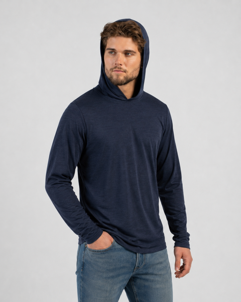 A man posing against a plain light background wearing a lightweight, long-sleeve navy blue hoodie with the hood pulled up over his head and blue jeans, with his right hand resting in his pocket.