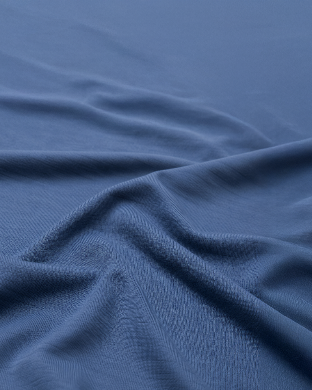 A close-up view of soft, dark blue fabric gently draped to show its smooth texture and rippling folds.