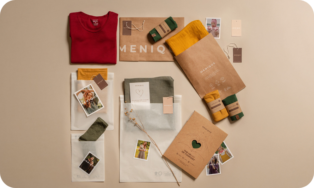 Colección de ropa y accesorios sobre una superficie beige con la marca 'MENIQ'.