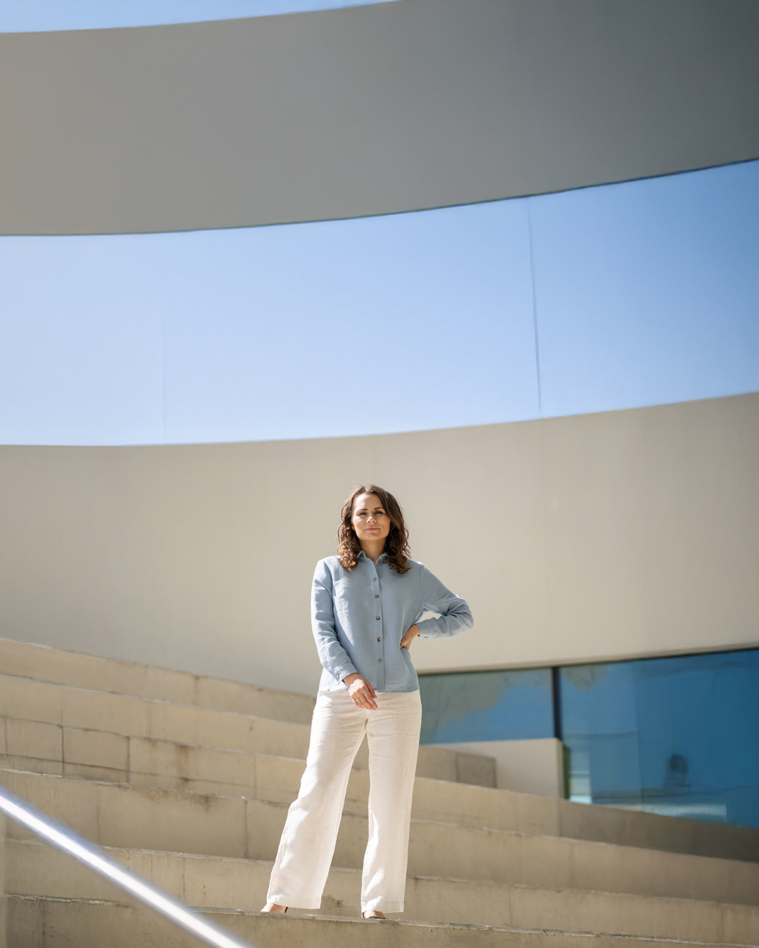 Mujer de pie en una escalera arquitectónica moderna con un cielo azul claro.