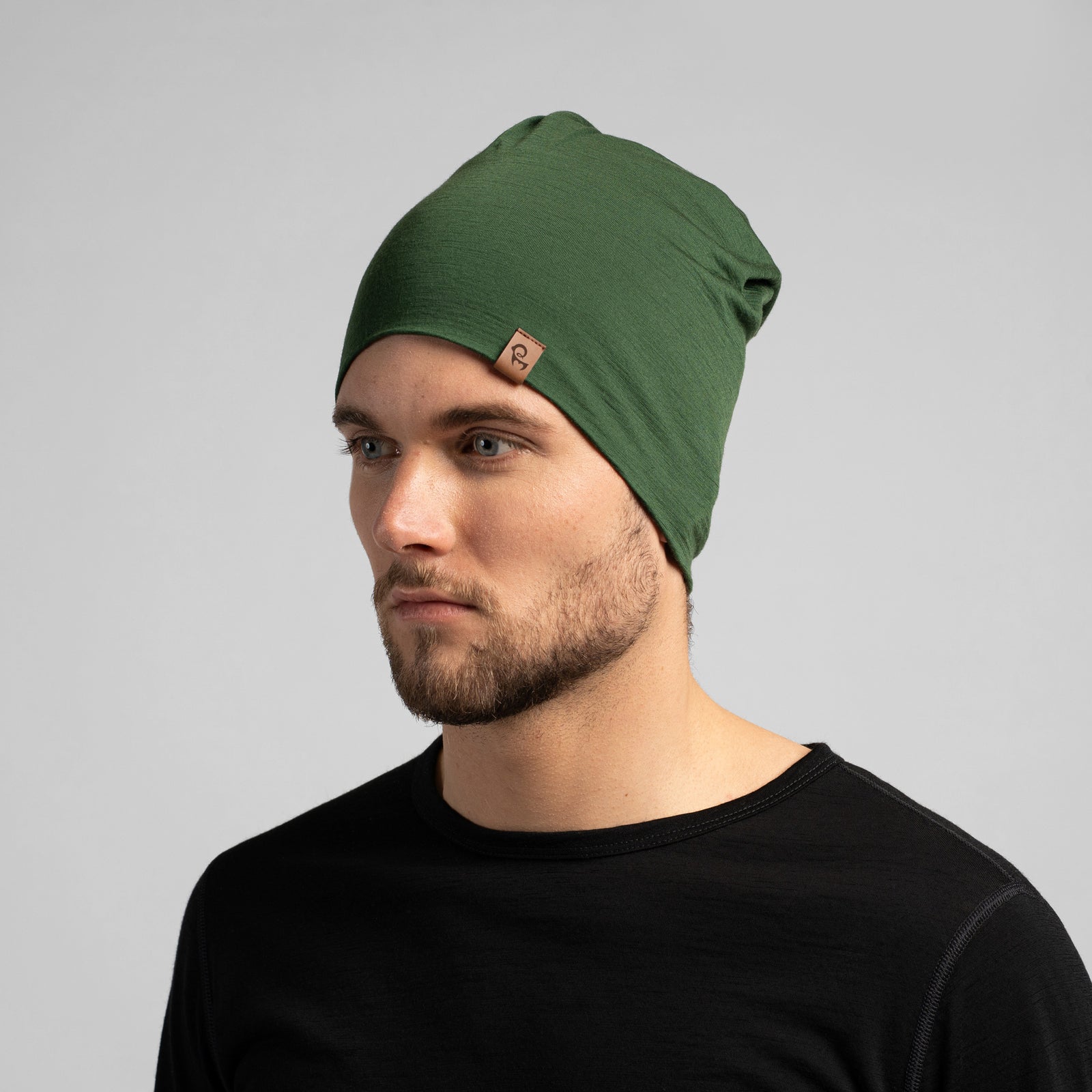 Una imagen de medio cuerpo de una pareja que lleva cintas para la cabeza unisex de merino Menique en verde oscuro. Están sonriendo, la mujer se apoya en el hombro del hombre. También llevan puestos suéteres de manga larga de merino en negro.
