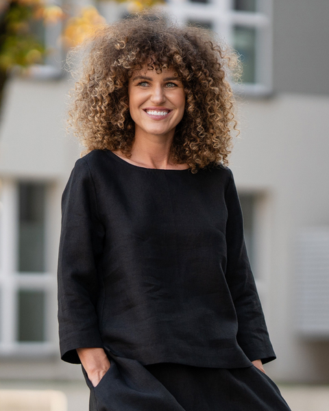 Mujer con una blusa negra de lino de pie al aire libre con fondo desenfocado