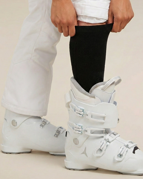 Primer plano de calcetines negros de esquí usados con botas de esquí blancas, mostrando un ajuste ceñido y longitud hasta la rodilla para deportes de invierno.