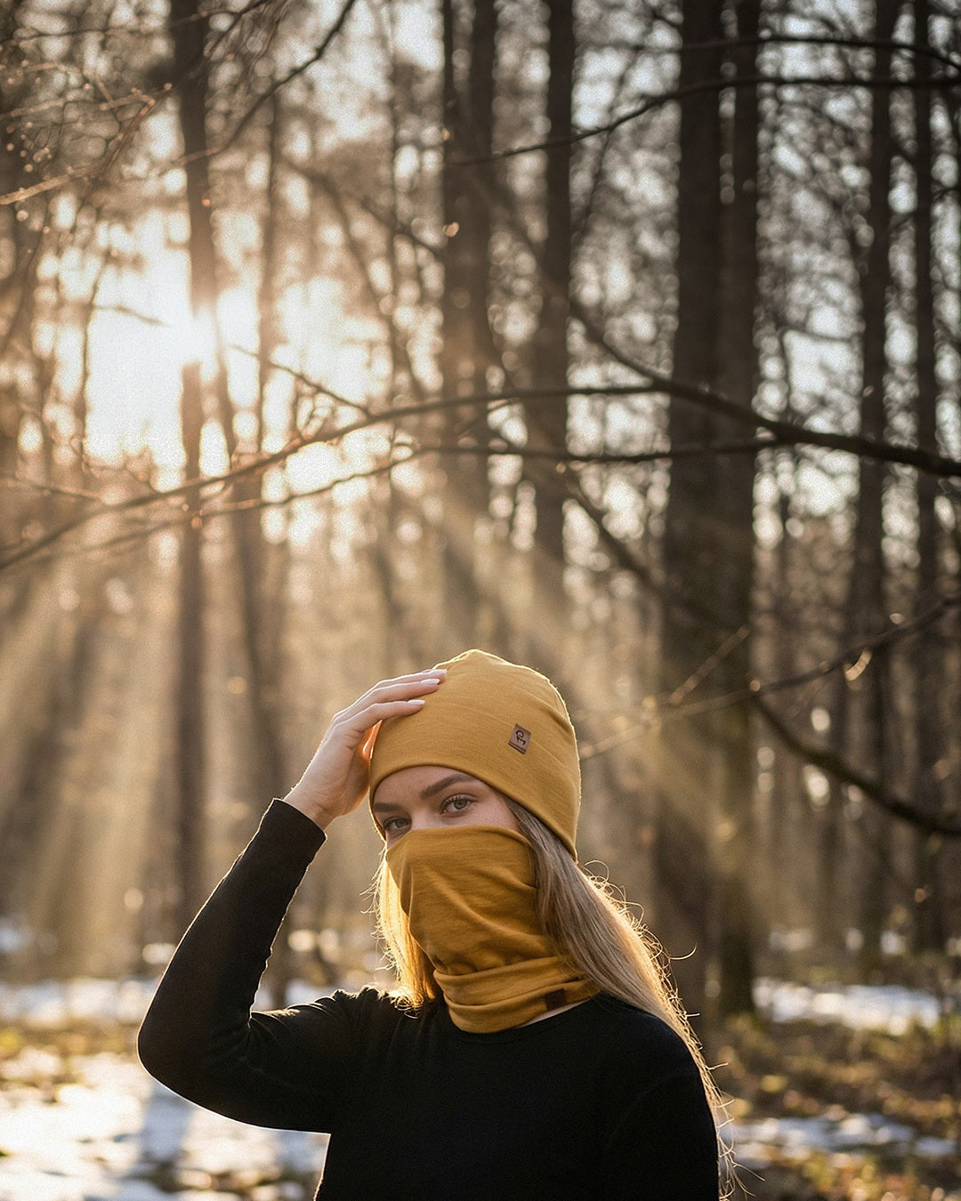 Woman wearing merino wool beanie and neck gaiter outdoors in a forest during cold weather.
